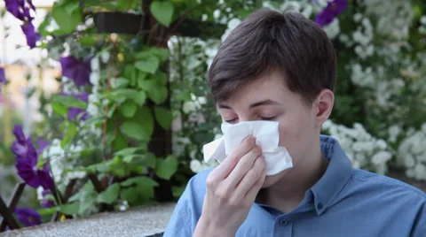 Teenager blowing nose,allergy season,pollen, young man sneezing in flower garden Stock Footage 39655710