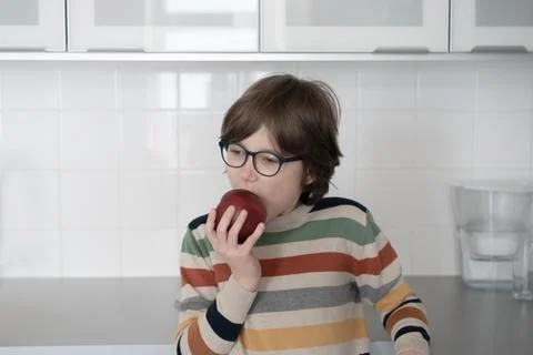 Teenager eats a red apple at home in the kitchen Stock Photos