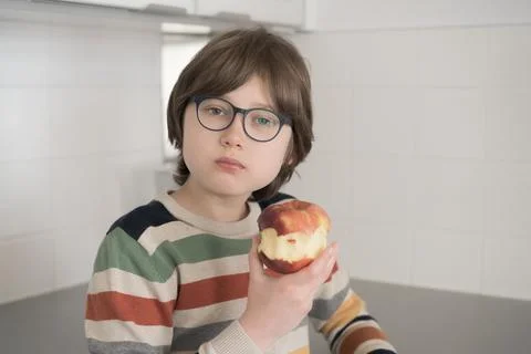 Teenager eats a red apple at home in the kitchen Stock Photos