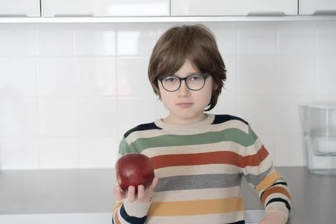 Teenager eats a red apple at home in the kitchen Stock Photos