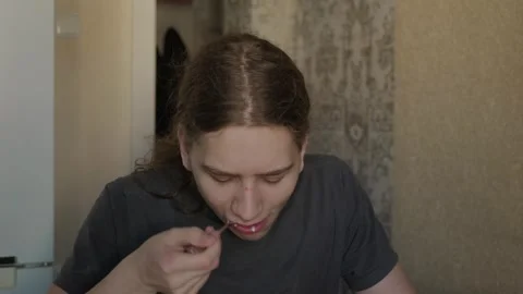 Teenager eats from spoon with focused downward gaze Stock Footage 341776121