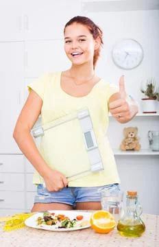 Teenager girl looking satisfied and holding scale on kitchen Stock Photos