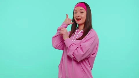 Teenager girl in pink hoodie looking at camera doing phone gesture like says hey Stock Footage