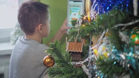 A teenager is playing with a tablet while sitting behind a Christmas tree. New Stock Footage 167797036