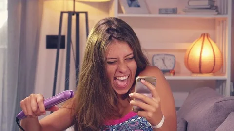 Teenager reading text message while straightening hair slow motion Stock Footage 84456099