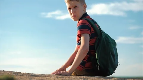 Teenager in a red shirt with a backpack behind him, at sunset, sitting on a high Stock Footage 108773553