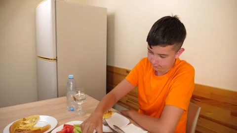 A teenager sits at a table, eats and drinks water. Stock Footage 319985137
