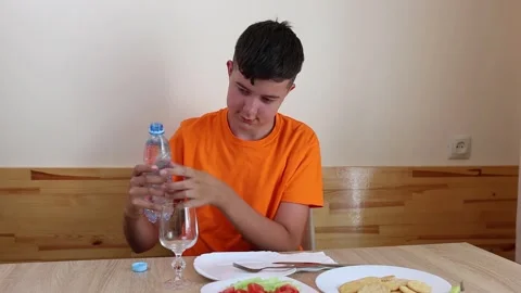 A teenager sits at a table, eats and drinks water. Stock Footage 319985196