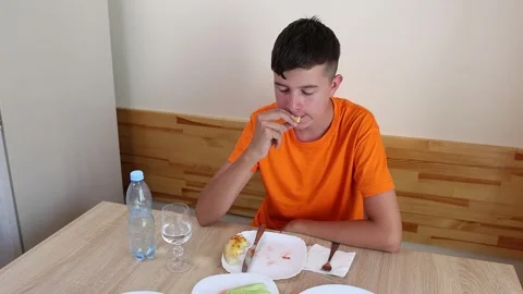 A teenager sits at a table, eats and drinks water. Stock Footage 319985203