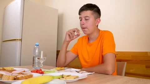 A teenager sits at a table, eats and drinks water. Stock Footage 320413710