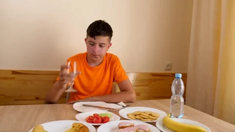 A teenager sits at a table, eats and drinks water. Stock Footage 320413725