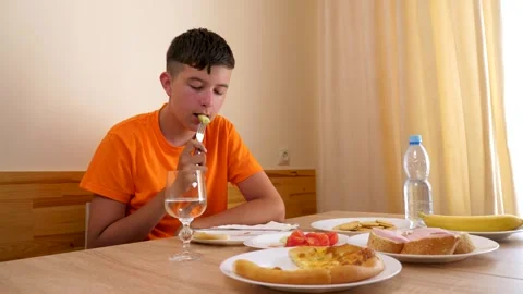 A teenager sits at a table, eats and drinks water. Stock Footage 320413729