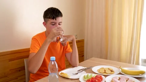 A teenager sits at a table, eats and drinks water. Stock Footage 320413733