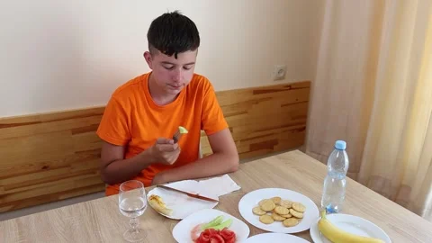 A teenager sits at a table, eats and drinks water. Stock Footage 321307534