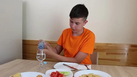 A teenager sits at a table, eats and drinks water. Stock Footage 321307535
