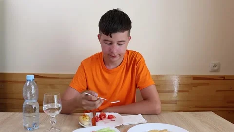 A teenager sits at a table, eats and drinks water. Stock Footage 321307540
