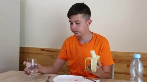 A teenager sits at a table, eats and drinks water. Stock Footage 321307549