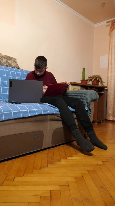 Teenager is sitting on a couch, using a tablet beside a laptop while studying Stock Footage 340517858