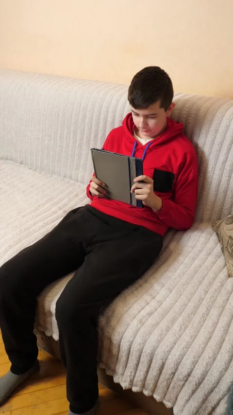 A teenager uses a tablet while sitting on a couch. Video stock 313486067