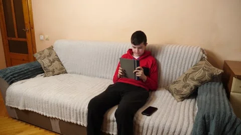 A teenager uses a tablet while sitting on a couch. Video stock 313486068