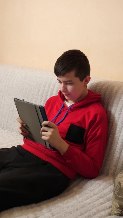 A teenager uses a tablet while sitting on a couch. Video stock 313486098