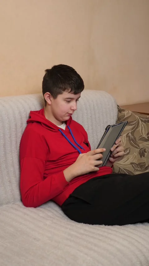 A teenager uses a tablet while sitting on a couch. Video stock 313486176