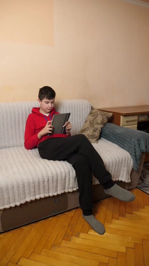 A teenager uses a tablet while sitting on a couch. Video stock 313486186