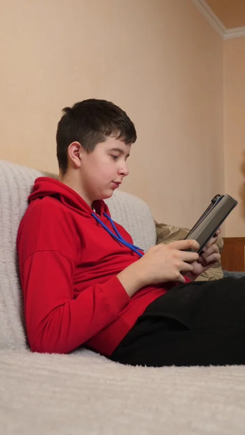 A teenager uses a tablet while sitting on a couch. Video stock 313729293