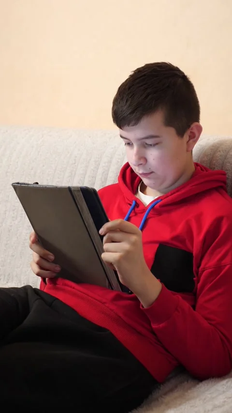 A teenager uses a tablet while sitting on a couch. Video stock 313729518