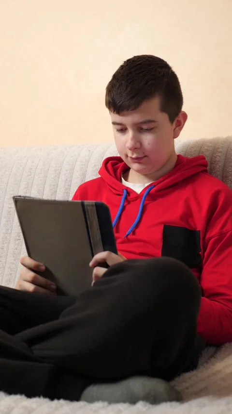 A teenager uses a tablet while sitting on a couch. Video stock 313729548