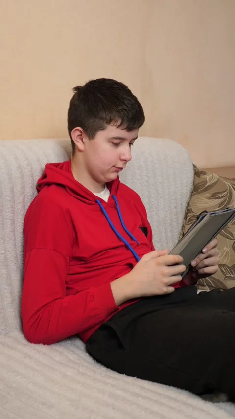 A teenager uses a tablet while sitting on a couch. Video stock 313729665