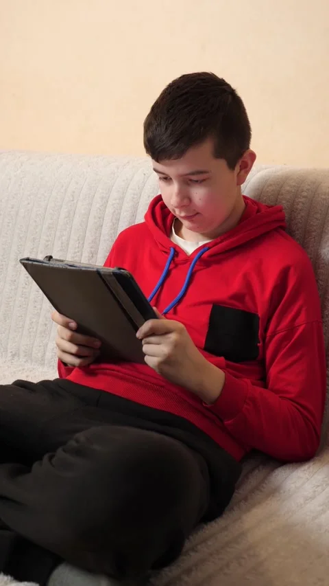 A teenager uses a tablet while sitting on a couch. Video stock 313982965
