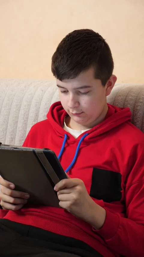 A teenager uses a tablet while sitting on a couch. Video stock 313982966