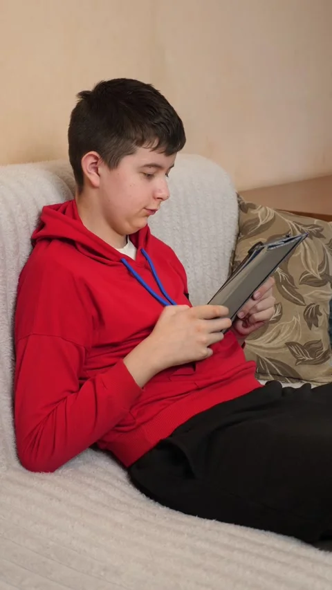 A teenager uses a tablet while sitting on a couch. Video stock 313983500