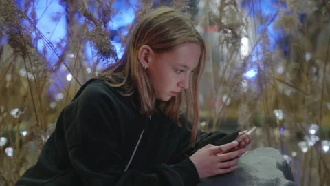 Teenager using smartphone while sitting by decorated plants in event Stock Footage 282546920