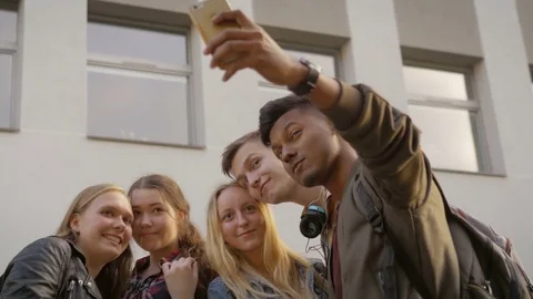 Teenagers smiling while taking selfies on phone by the school Stock Footage 74567030