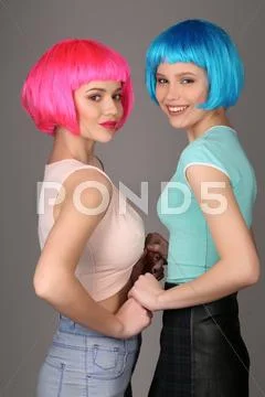 Teens In Colorful Wigs Holding Hands And Posing. Close Up. Gray Background