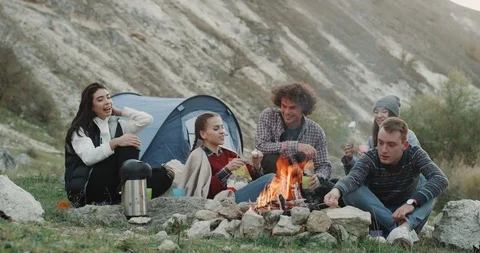 Teens have a nice camping time in front of bonfire , relaxing time drinking wine Stock Footage 98131494
