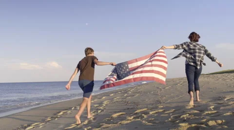 Teens Hold American Flag Between Them, They Run Down Beach, Away From Camera Stock-Footage 57414729