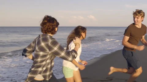 Teens Make A Game Of Running Away From Waves On Beach Stock Footage
