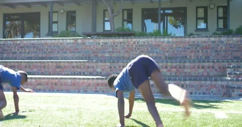 Teens pushing off, practicing cartwheels, handstanding on lawn by brick wall, Stock Footage 344326102