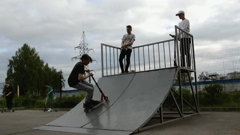 Teens on scooters performs a tricks in the skatepark Stock Footage 132927417