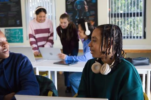 Teens working in class around laptop, teen with braided hair wearing headset Stock Photos