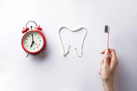 Teeth brushing concept. Toothbrush in the hand of a young woman and an alarm  Stock Photos