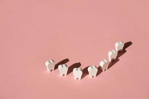 Teeth stand on a pink background in a row, forming a smile. Stock Photos