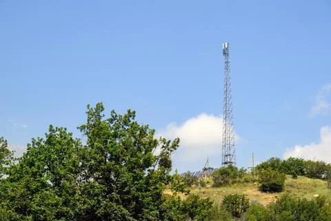 Telecom tower rising over grassy hill with trees below Stock Photos