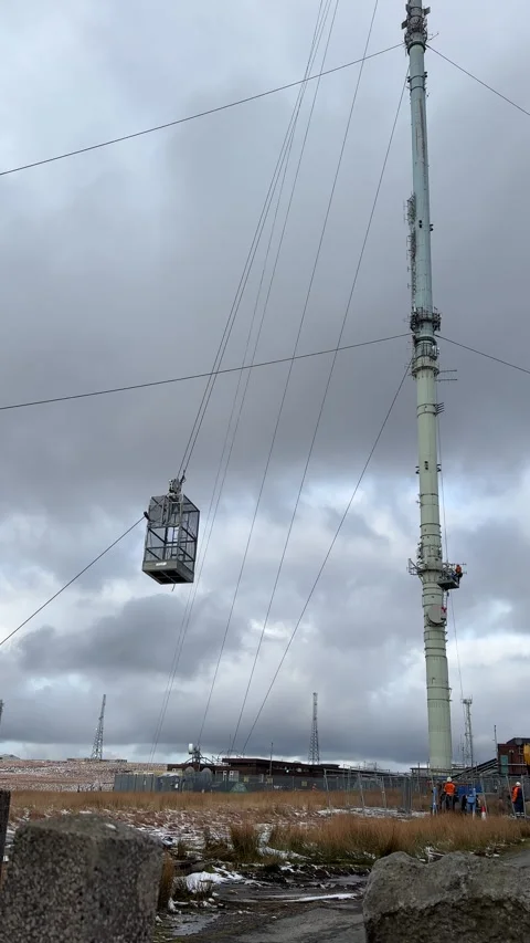Telecommunications tower technician going up in open air hoist carrying ladder. Stock-Footage 331305439