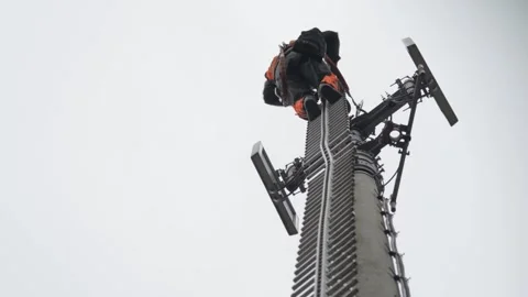 Telecommunications Worker Climbing Cell Tower for Maintenance on Overcast Day Stock Footage 334053718