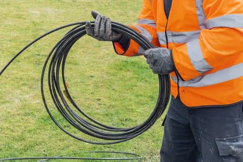 Telecoms engineer coiling fibre optic cable over grass at works Stock Photos