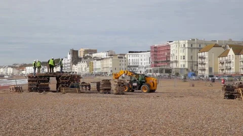 Telehandler builds bonfire from wooden pallets on stony beach in Hastings Stock Footage 136473680